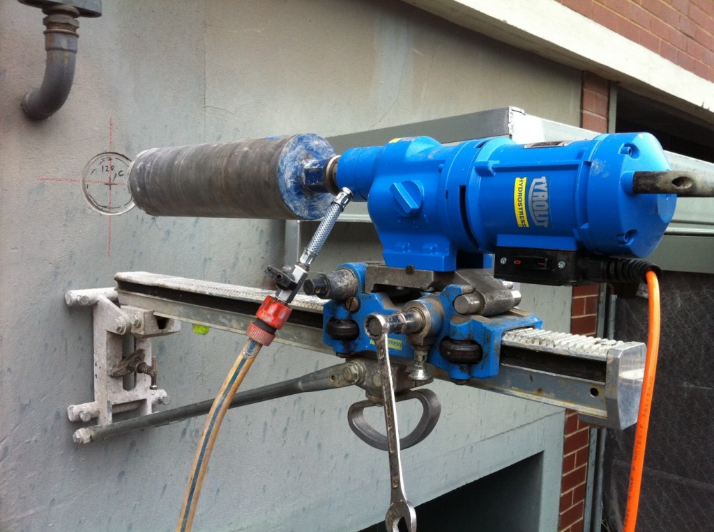 Bolt-down core drilling rig mounted on exterior concrete wall for precision drilling