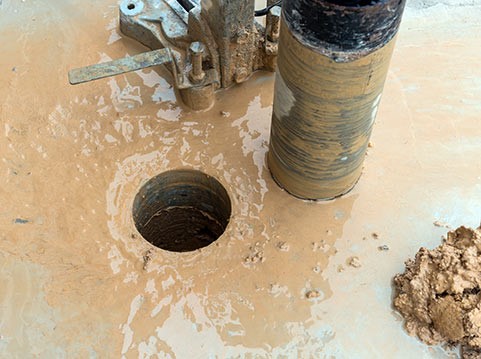 Completed core drill hole in concrete slab with extracted core and slurry
