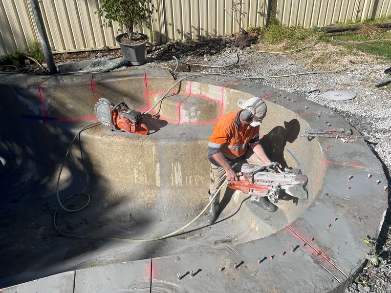 Concrete cutting worker using hand saw for pool demolition and removal project