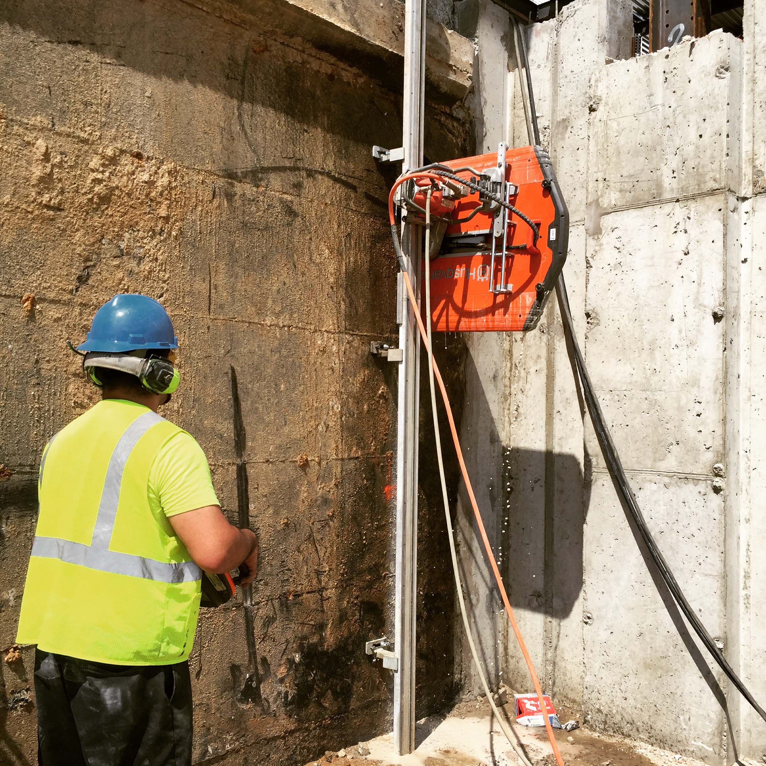 Track-mounted wall saw cutting through thick reinforced concrete wall on site
